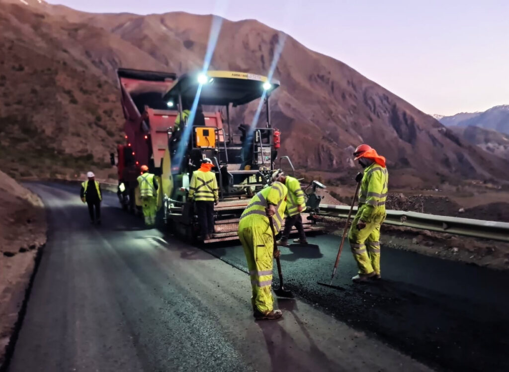 Hombres trabajando con máquinas en el pavimento de una carretera al atardecer